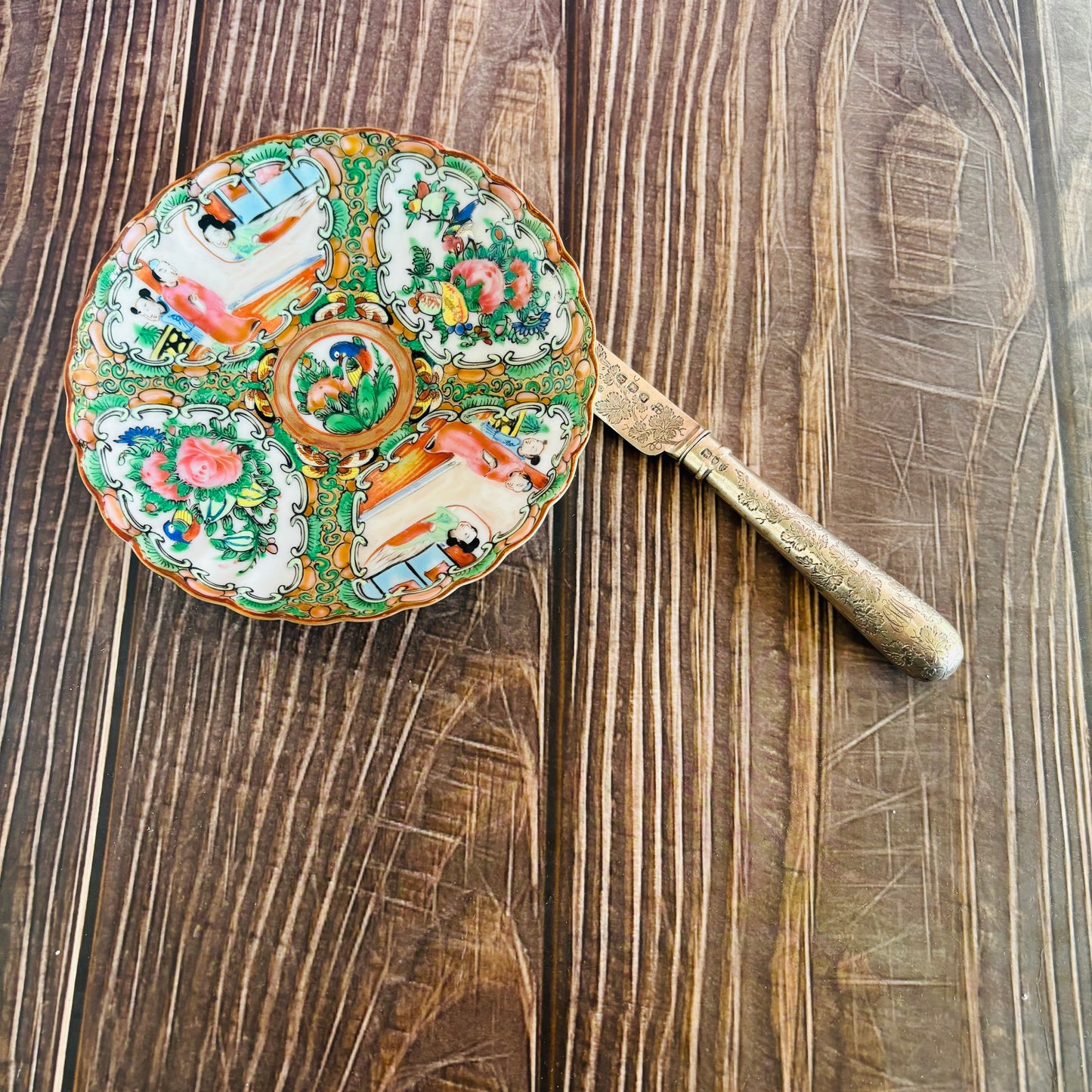 Antique Chinese Rose Medallion Pattern Saucer with intricate designs on a wooden surface next to s silver knife