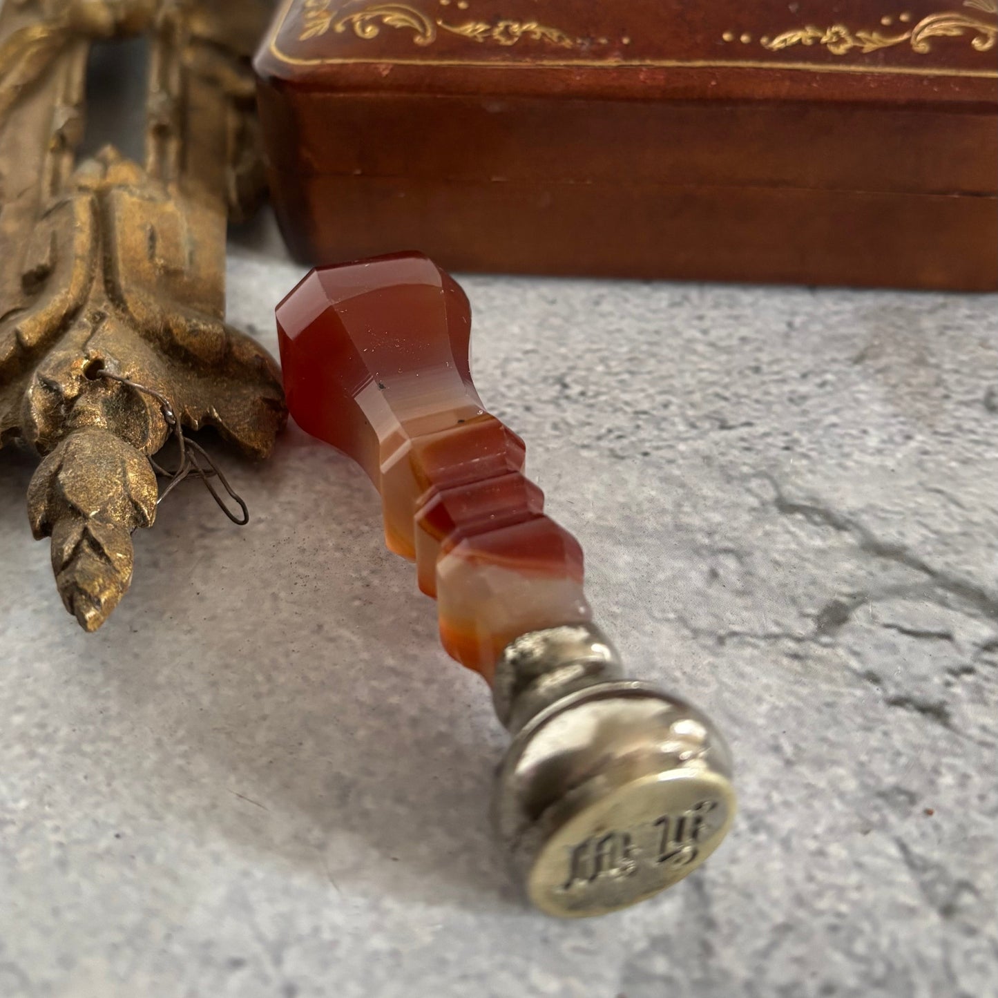 Decorative wax seal with agate stone handle and metal top on a textured surface
