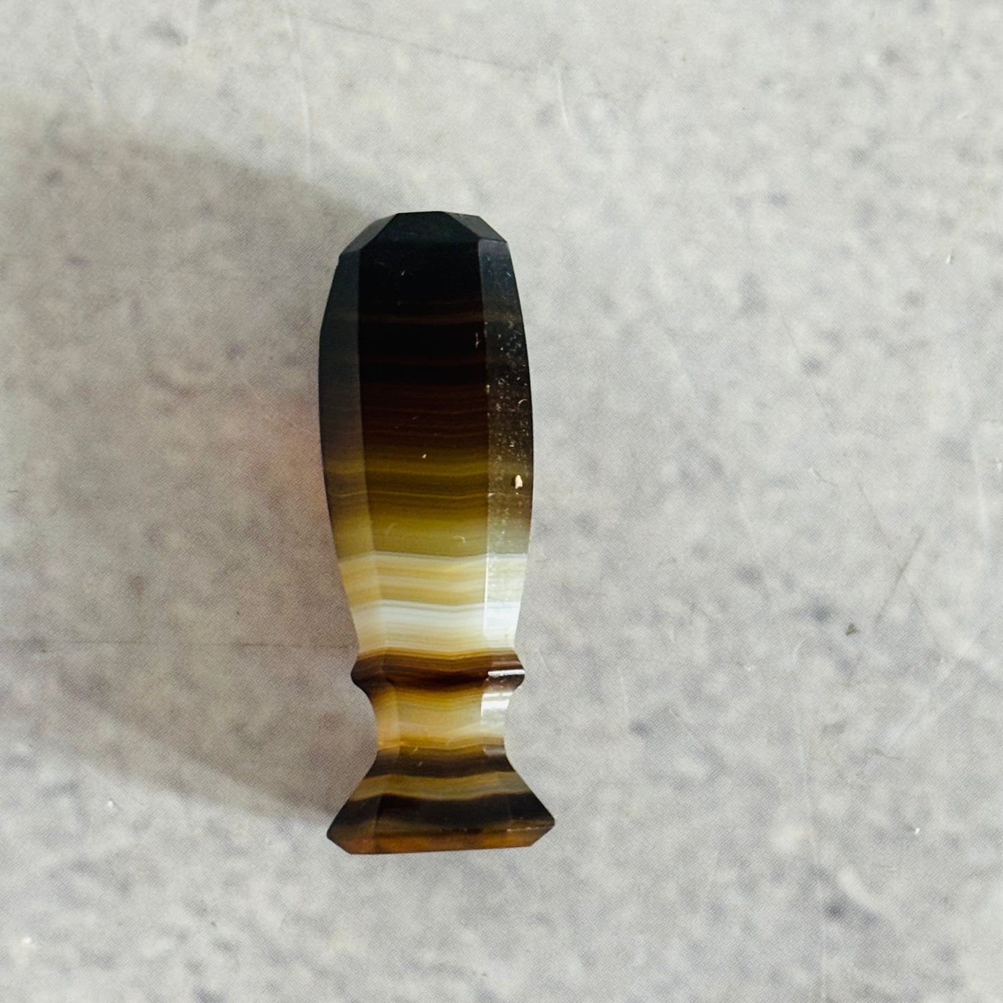 Faceted gemstone wax seal with brown and black coloration on a gray background
