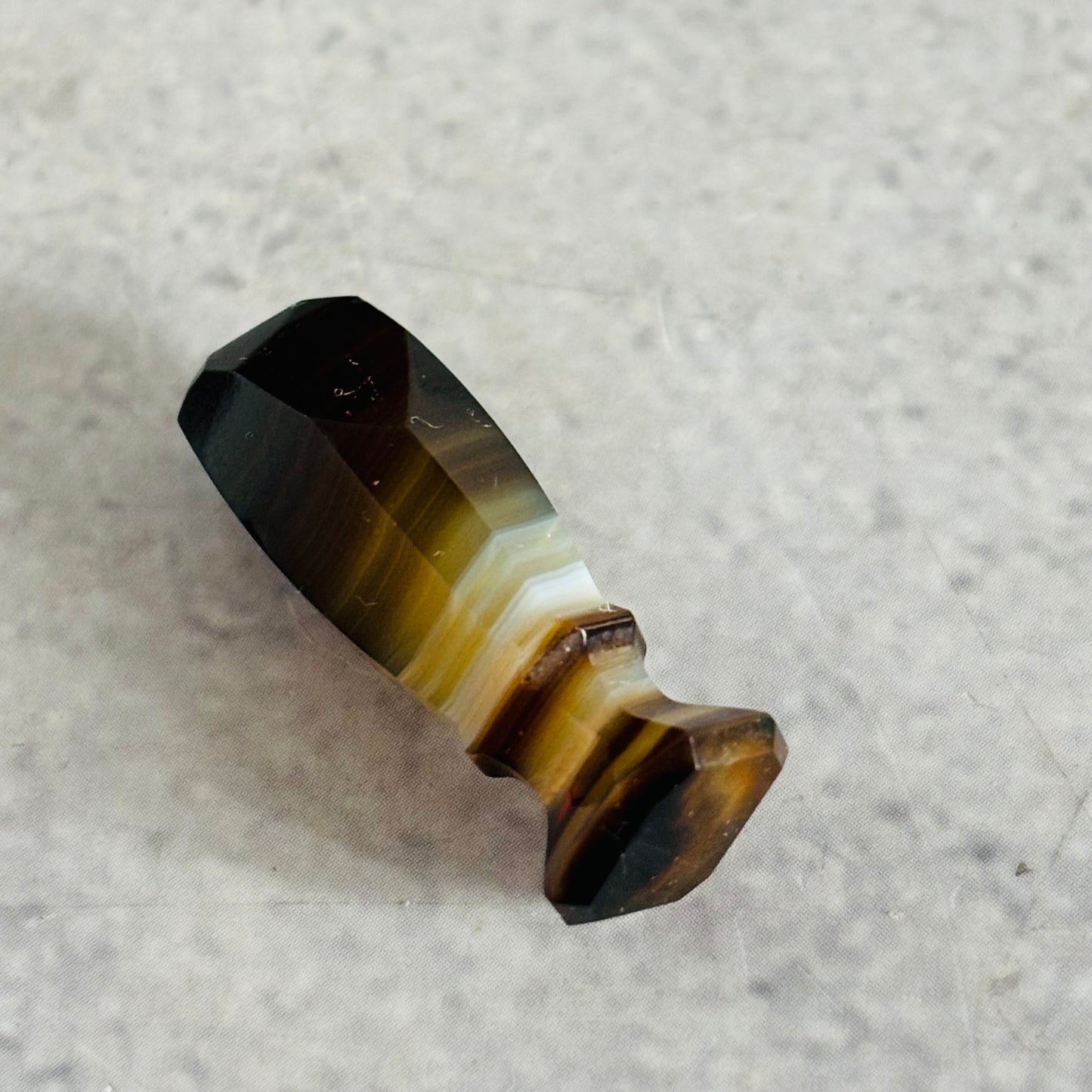 Polished crystal with brown and white stripes on a gray surface