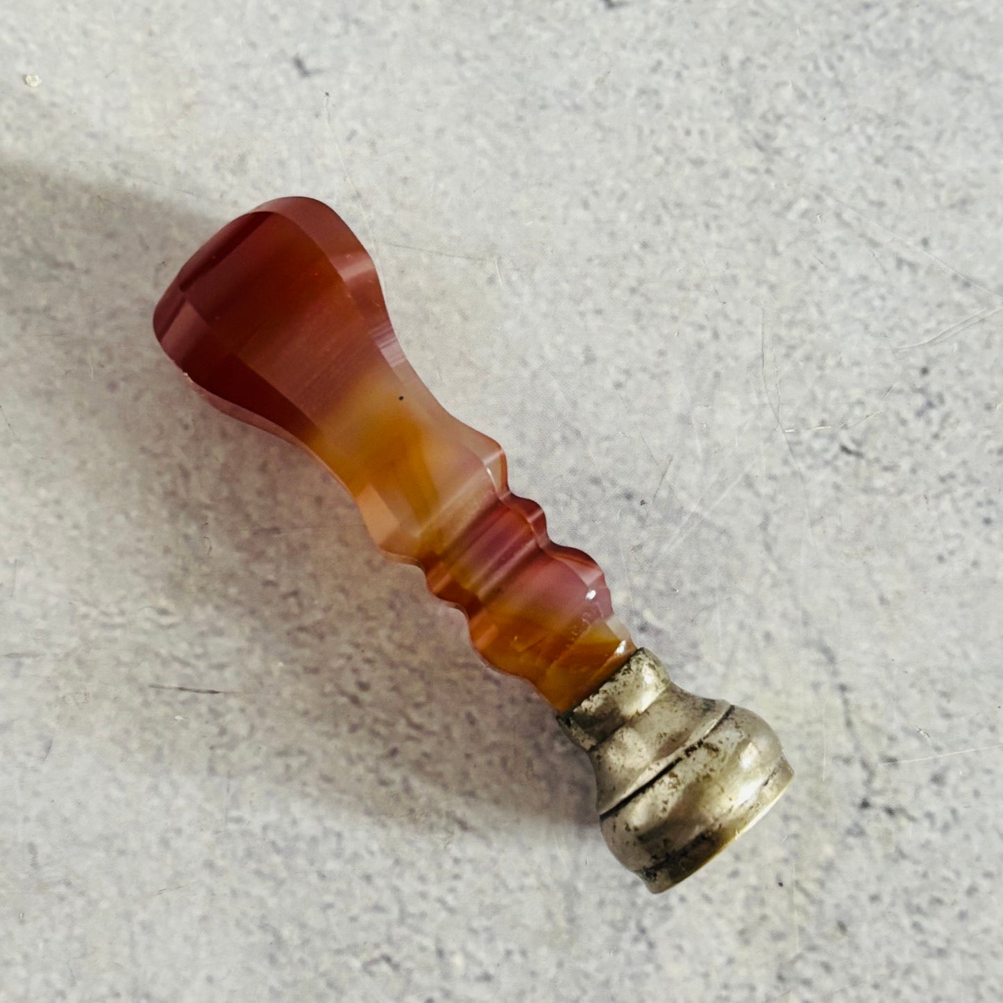 Marbled red and orange agate wax seal stamp with a metallic base on a textured grey surface
