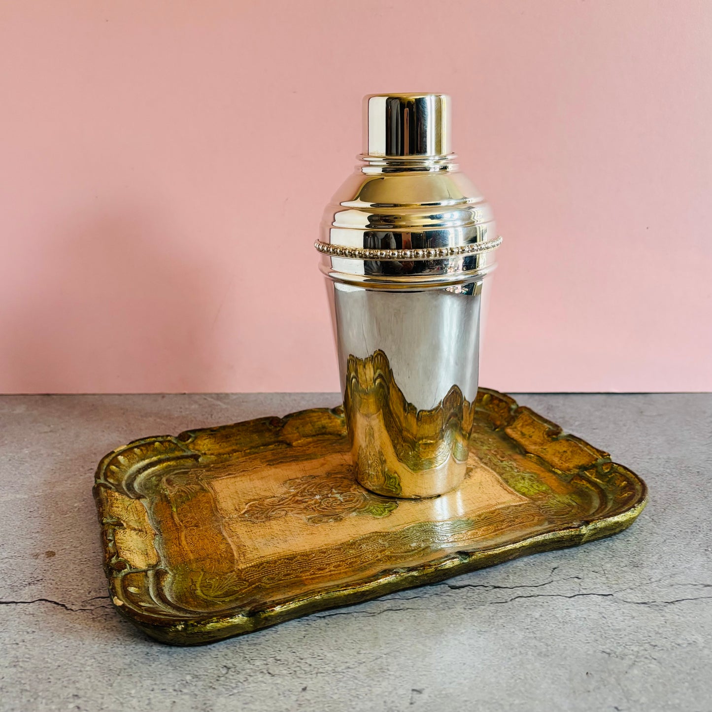 Silver cocktail shaker on a decorative wooden tray with a pink background