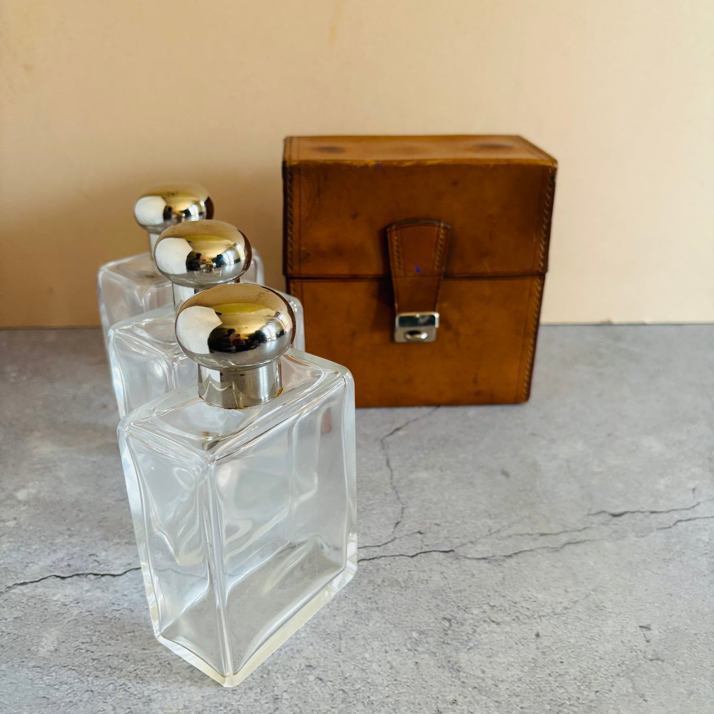 Three clear glass bottles with silver lids and a brown leather box on a gray surface.