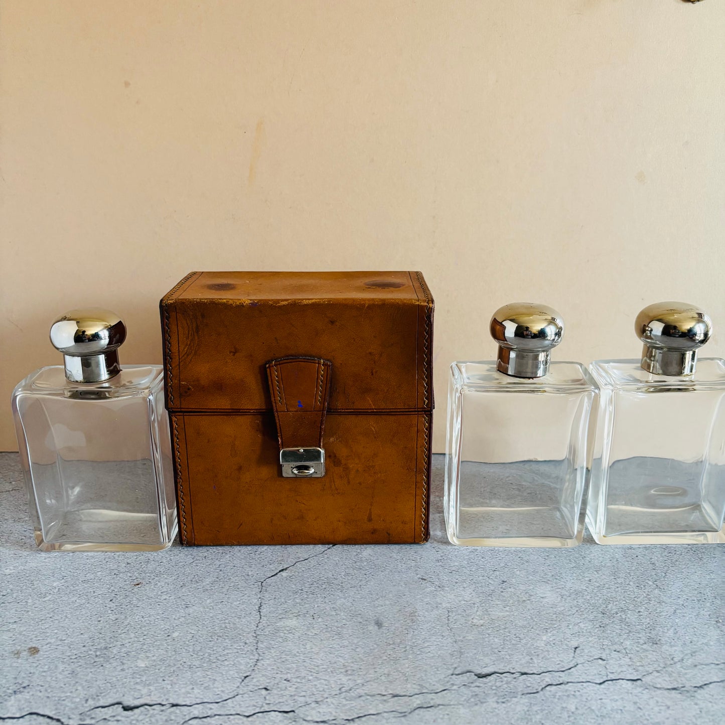 Three glass bottles with metal caps and a brown leather box on a textured surface.