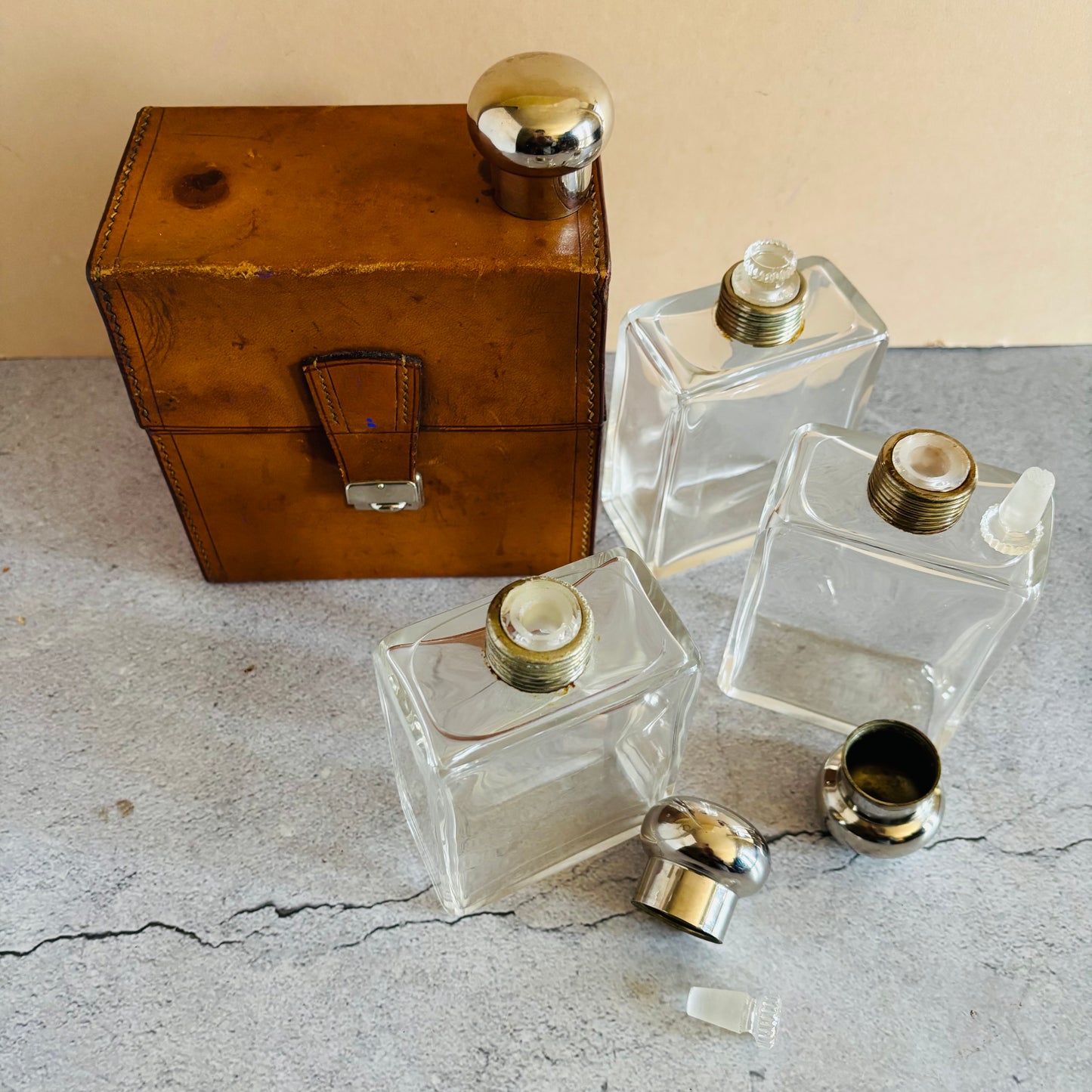 Three clear glass bottles with metal caps and a brown leather box on a textured surface.