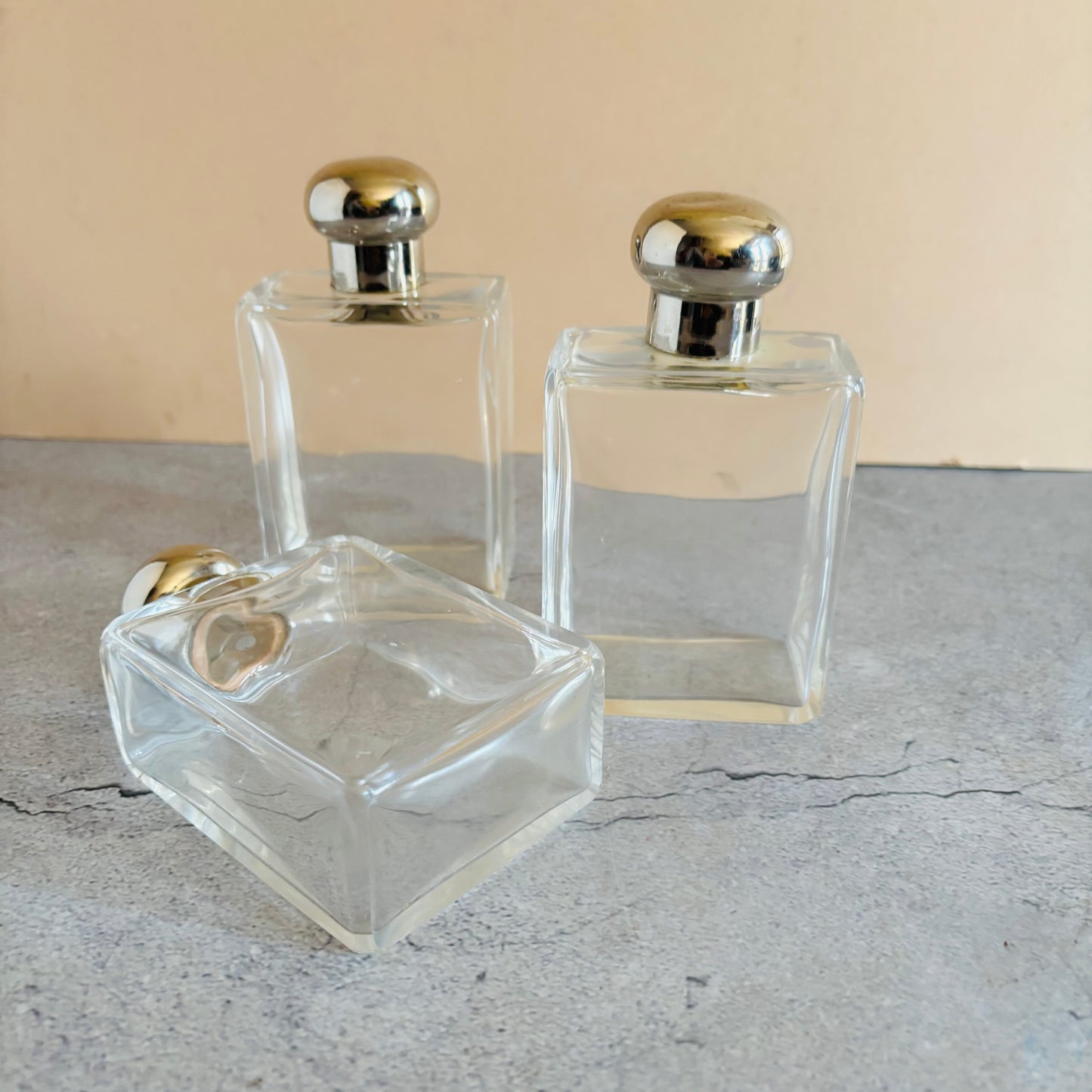 Three clear glass perfume bottles with silver tone caps on a grey surface.