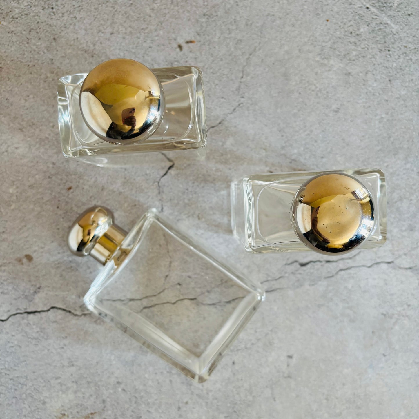 Three clear perfume bottles with silver caps on a grey marble surface