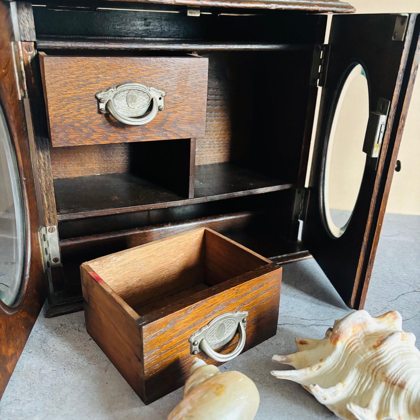 Wooden jewellery box with a drawer open, surrounded by seashells on a textured surface.
