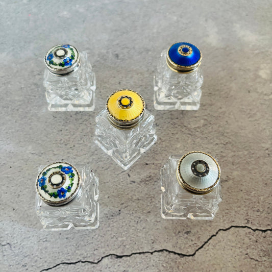 Five vintage small glass and silver guilloche enamel salt and pepper bottles with colourful stoppers on a grey surface
