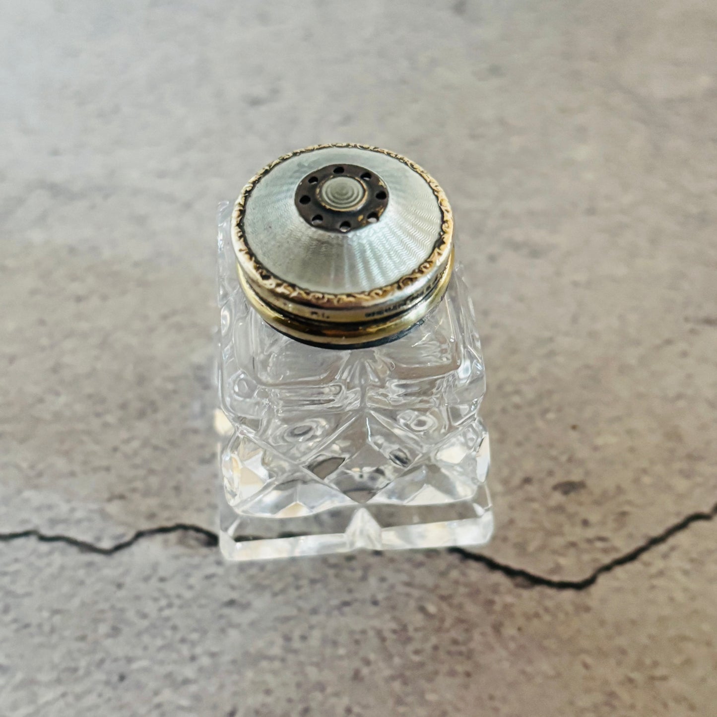 Glass and silver guilloche enamel salt and pepper bottle with colourful stopper on a grey surface