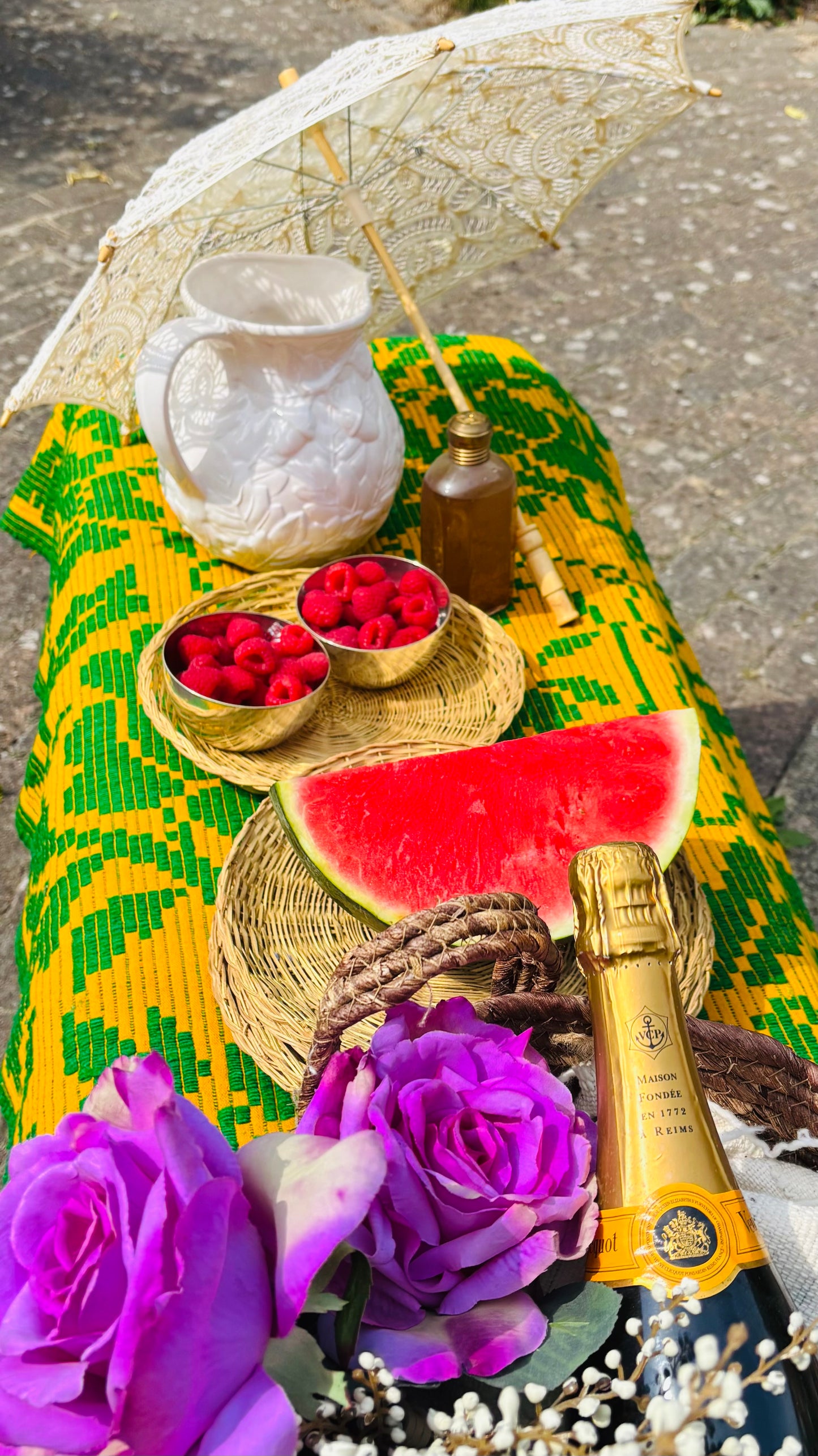 Table with watermelon, raspberries, and a bottle of champagne on a colorful tablecloth.