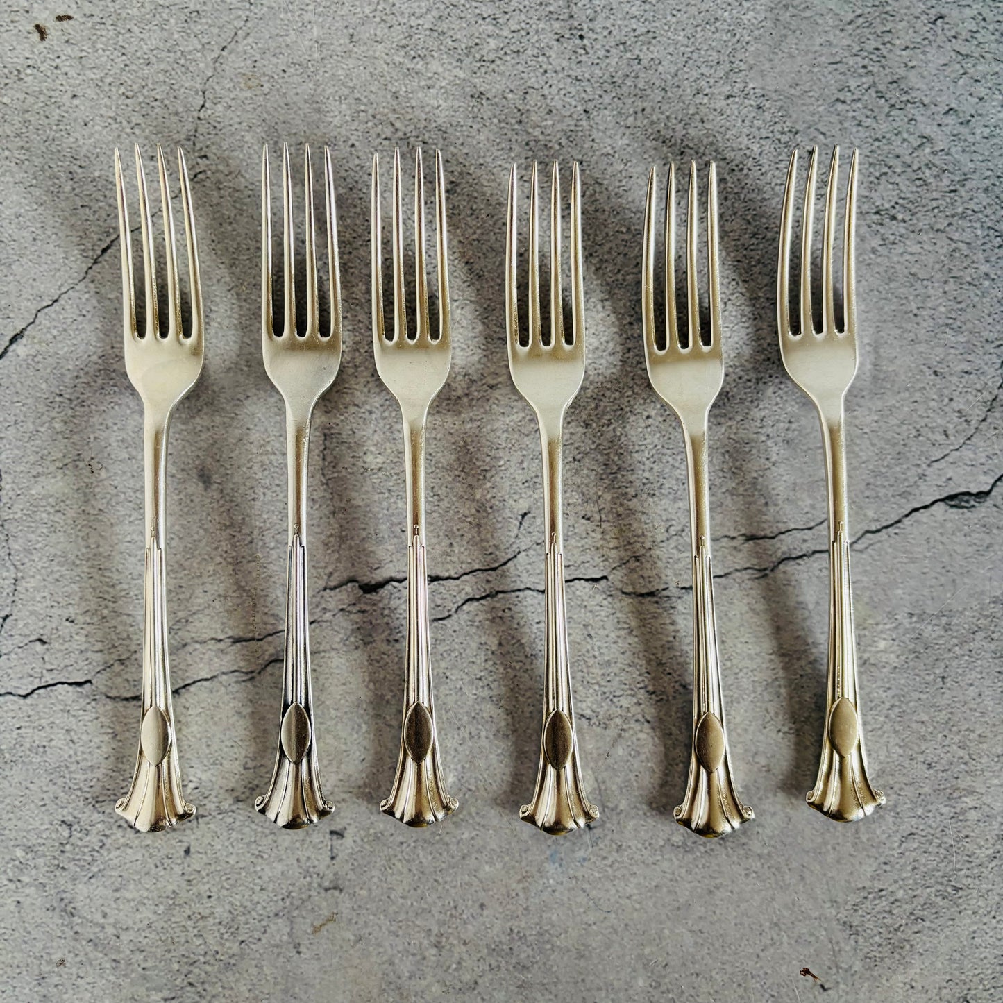 Set of six silver forks on a textured grey surface