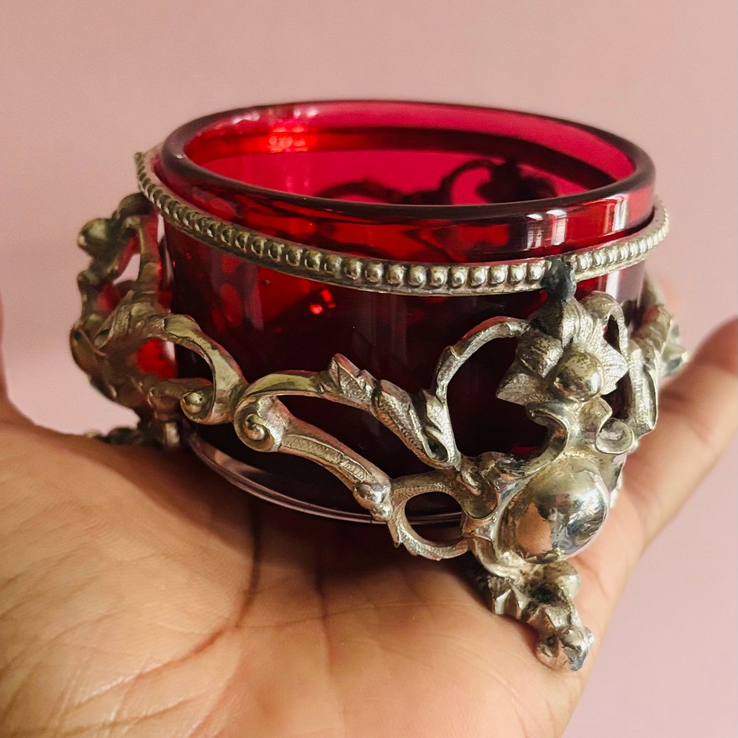 Decorative red glass with ornate silver metal base salt celler held in a hand against a pink background