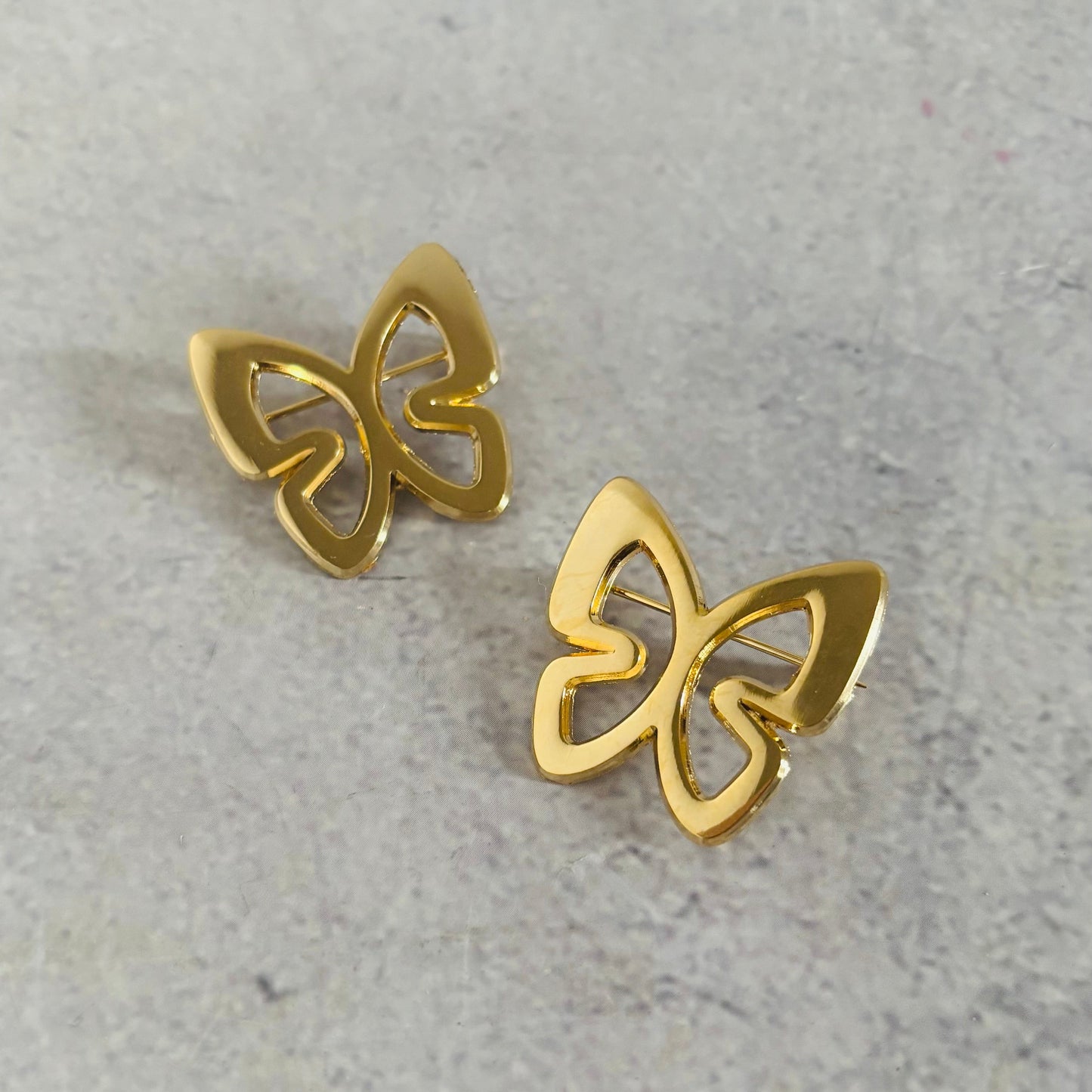 Gold butterfly earrings on a gray concrete surface