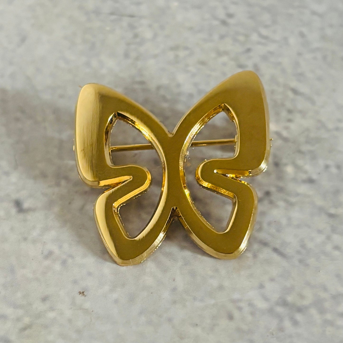 Gold butterfly-shaped pin badge on a light grey background