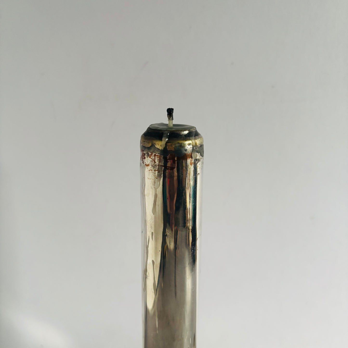 Tall cylindrical spring loaded candlestick with a metallic top on a grey background
