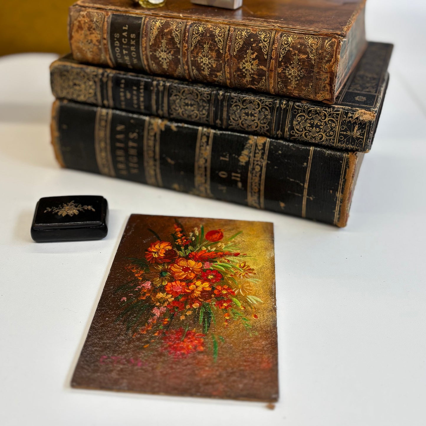 Stack of old books with a floral painting on a white surface