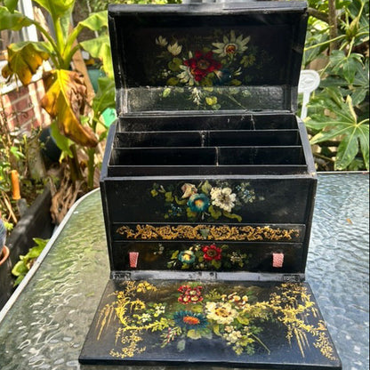 Victorian Paper Mache Lacquer Stationery Box  with hand painted floral patterns on a glass table outdoors.