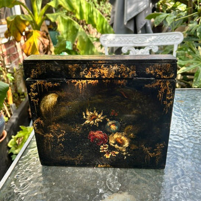 Victorian Paper Mache Lacquer Stationery Box  with hand painted floral patterns on a glass table outdoors.