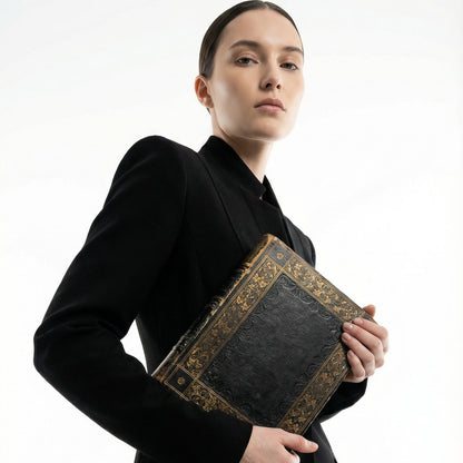 Person holding a black book with gold detailing against a white background