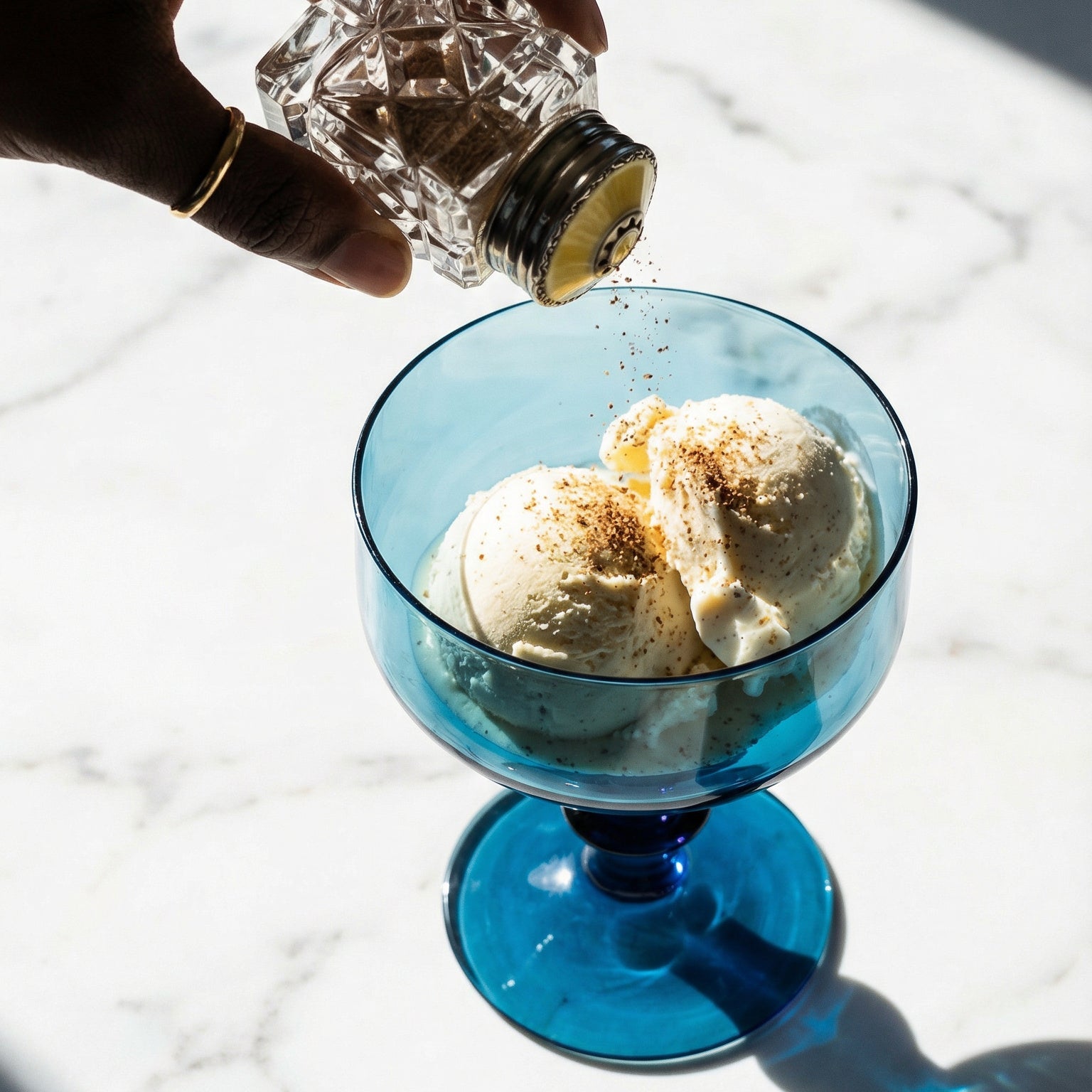 Hand pouring a clear liquid into a blue glass with ice cream on a marble surface
