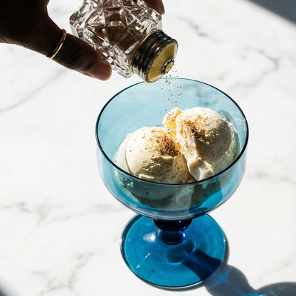 Hand pouring a clear liquid into a blue glass with ice cream on a marble surface
