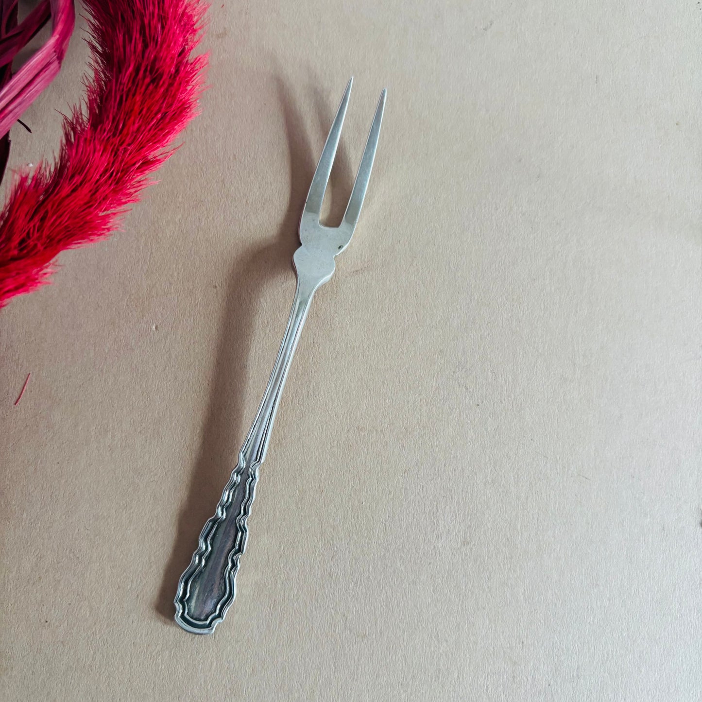 Silver decorative fork on a beige background with pink feathers