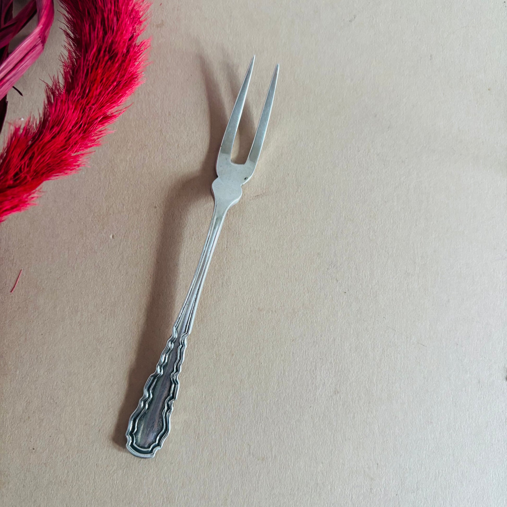Silver decorative fork on a beige background with pink feathers