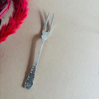Silver decorative fork on a beige background with pink feathers