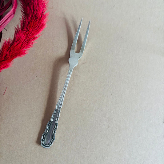 Silver decorative fork on a beige background with pink feathers