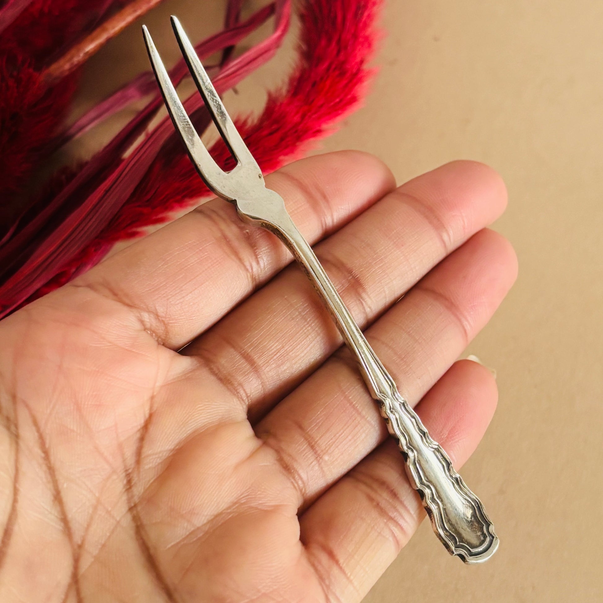 Silver decorative fork held in a hand with a red feather in the background
