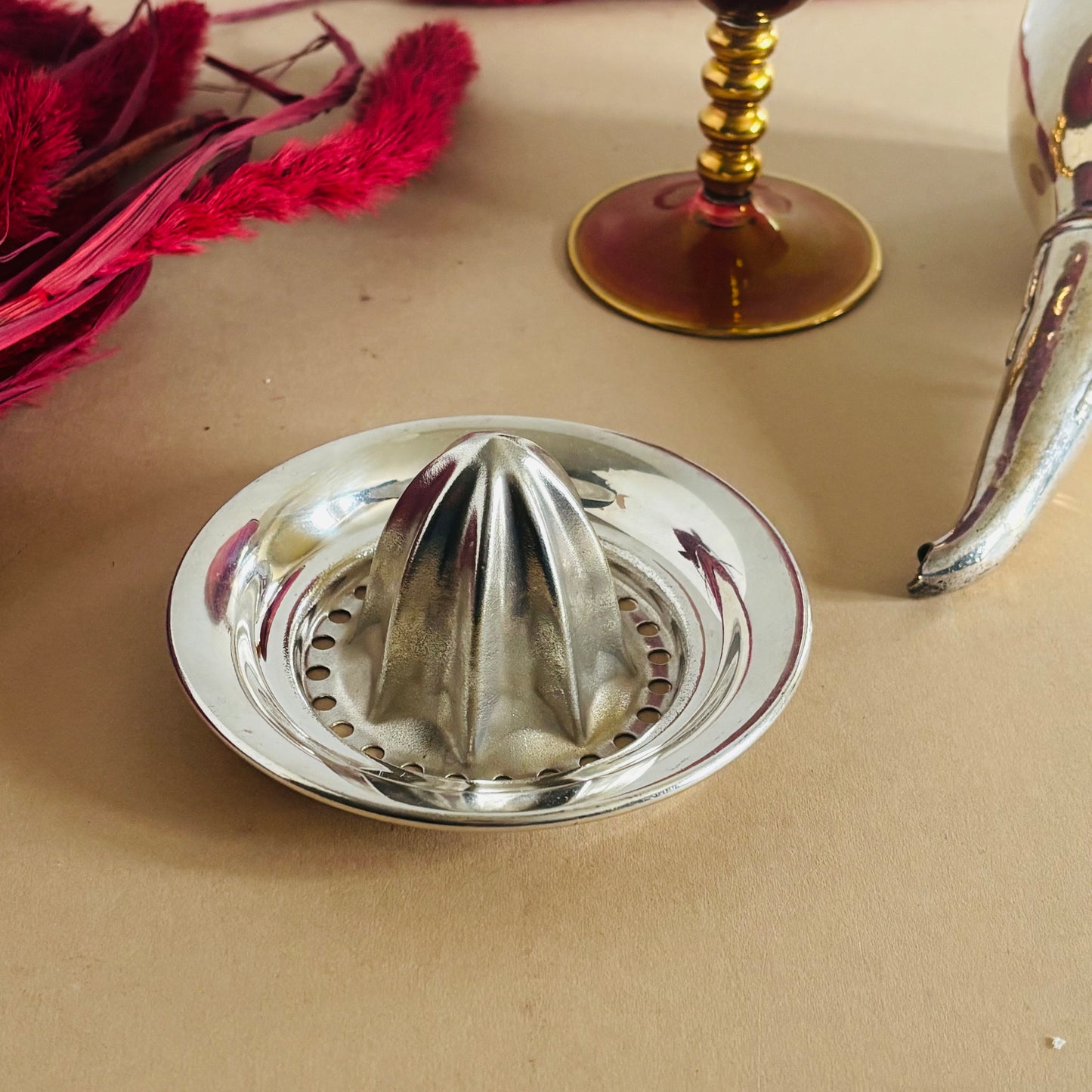 Silver manual juicer on a beige surface with decorative elements.