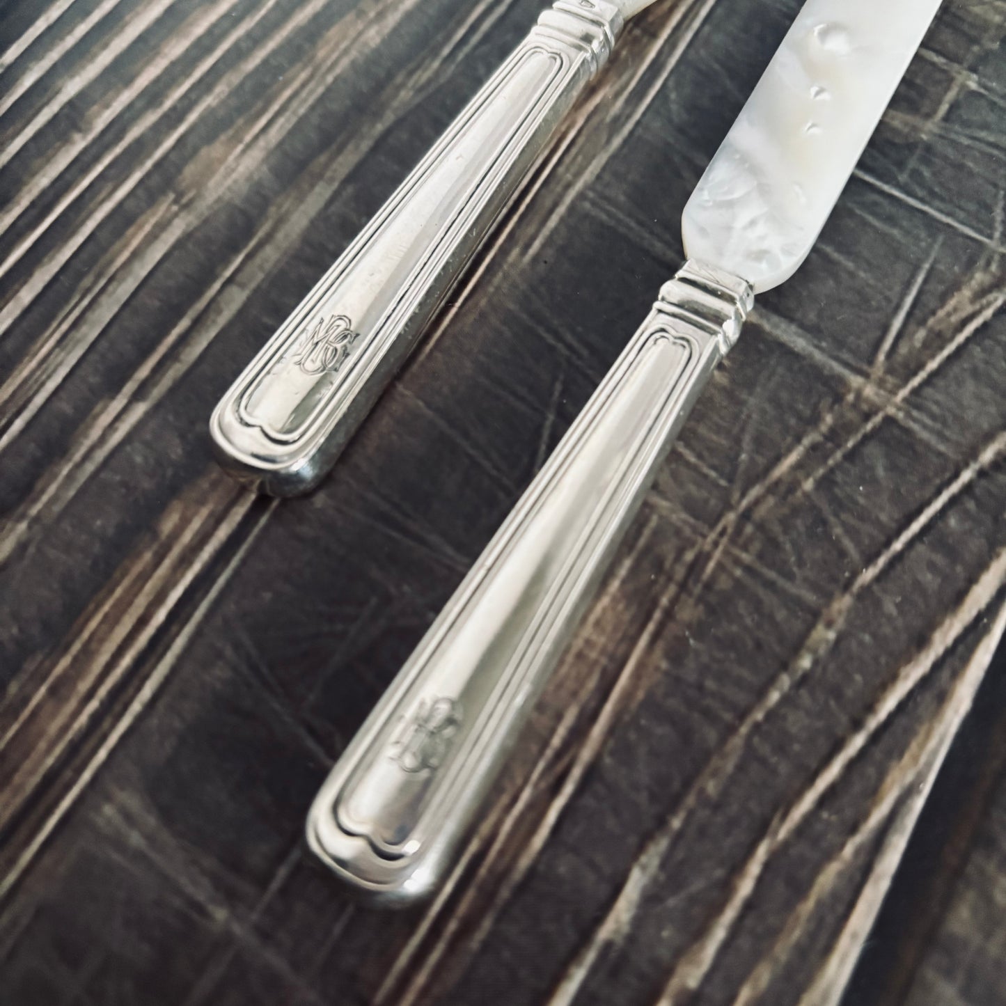 Two antique Silver & Mother Of Pearl Caviar knives  on a wooden surface