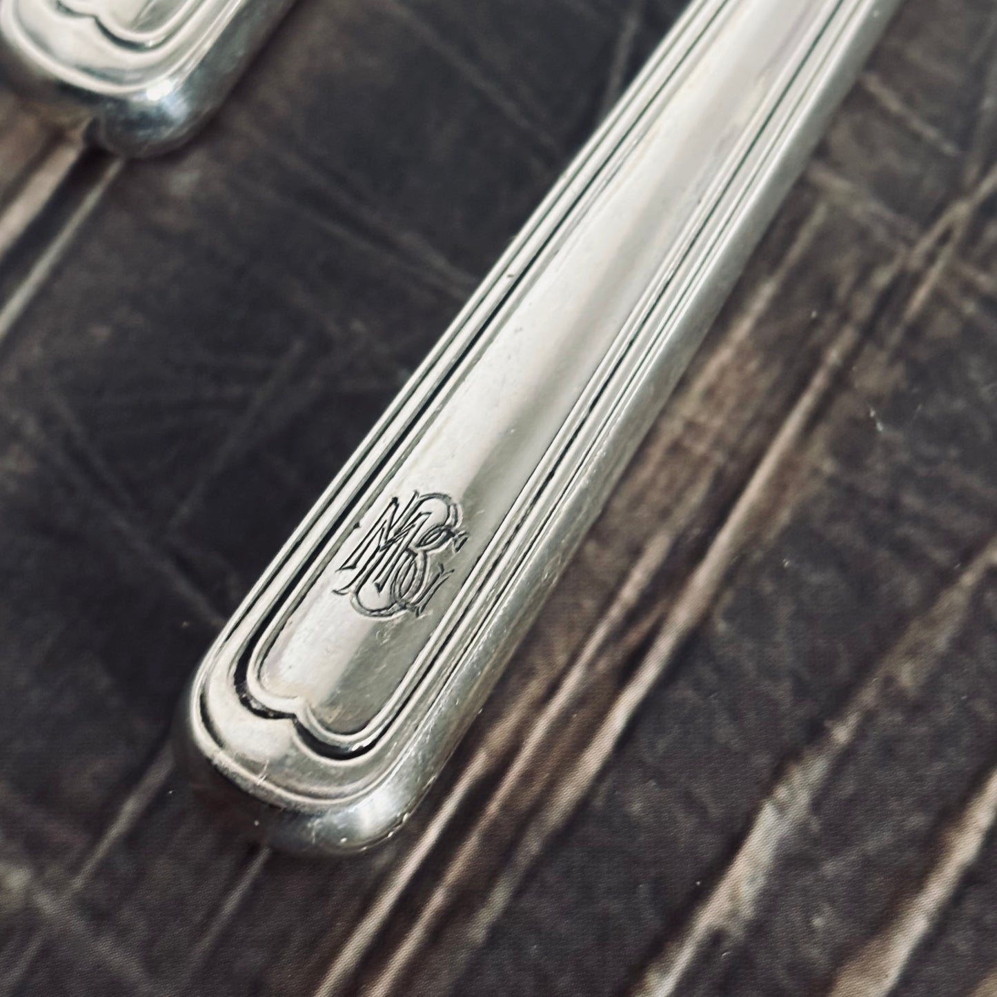 Close-up of a silver knife handle with engraved design on a dark wooden surface