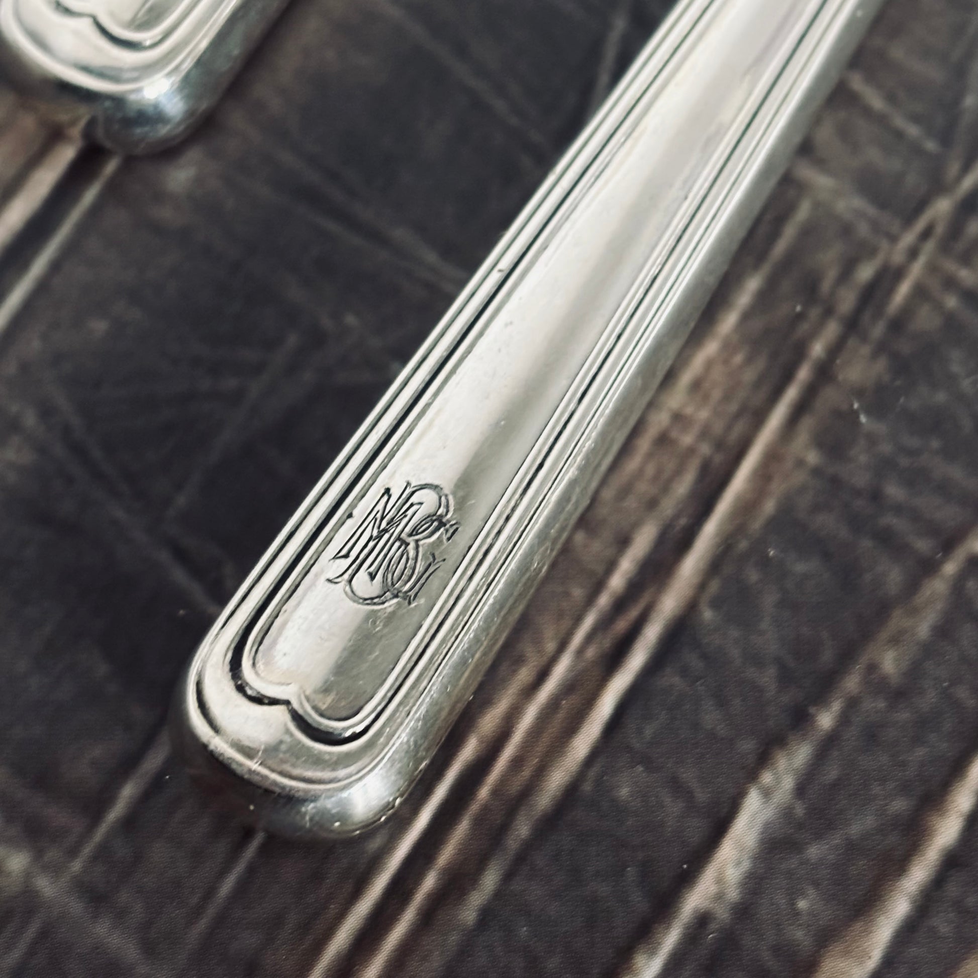 Close-up of a silver knife handle with engraved design on a dark wooden surface