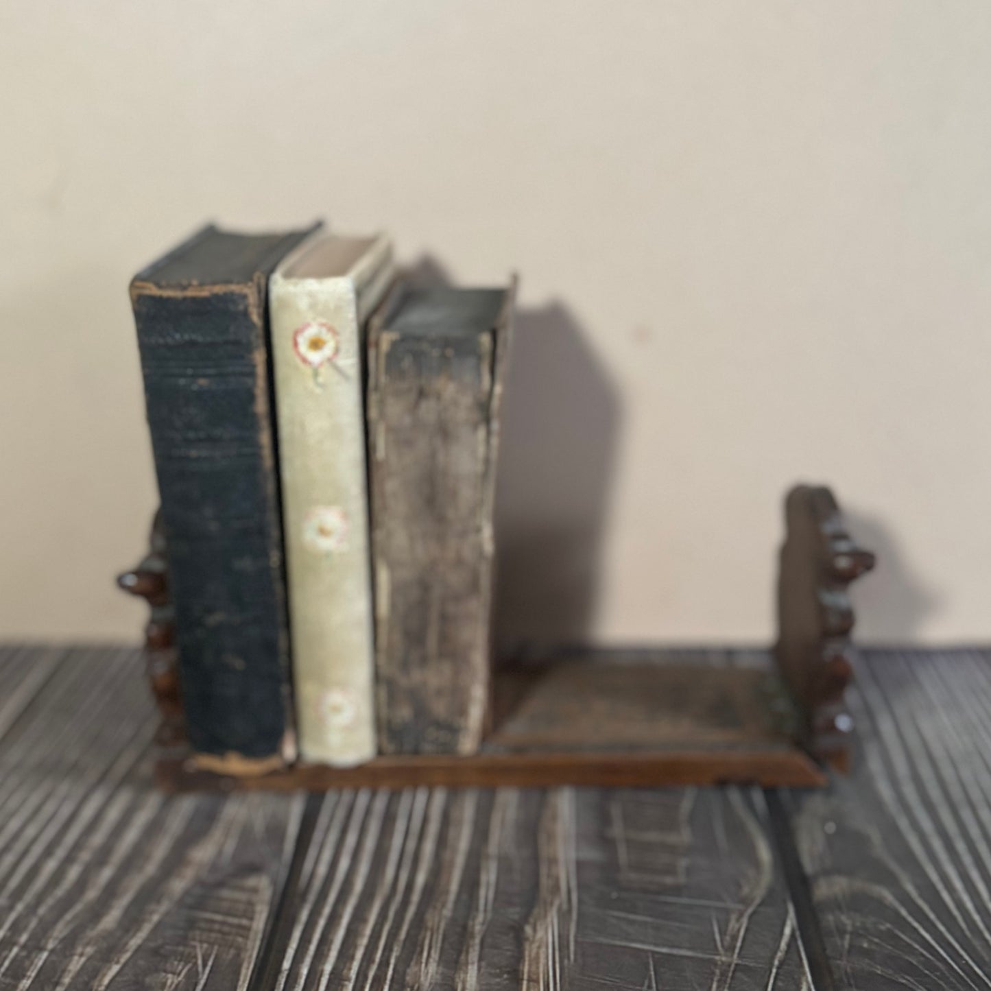 Three old books on a wooden book slide against a plain background