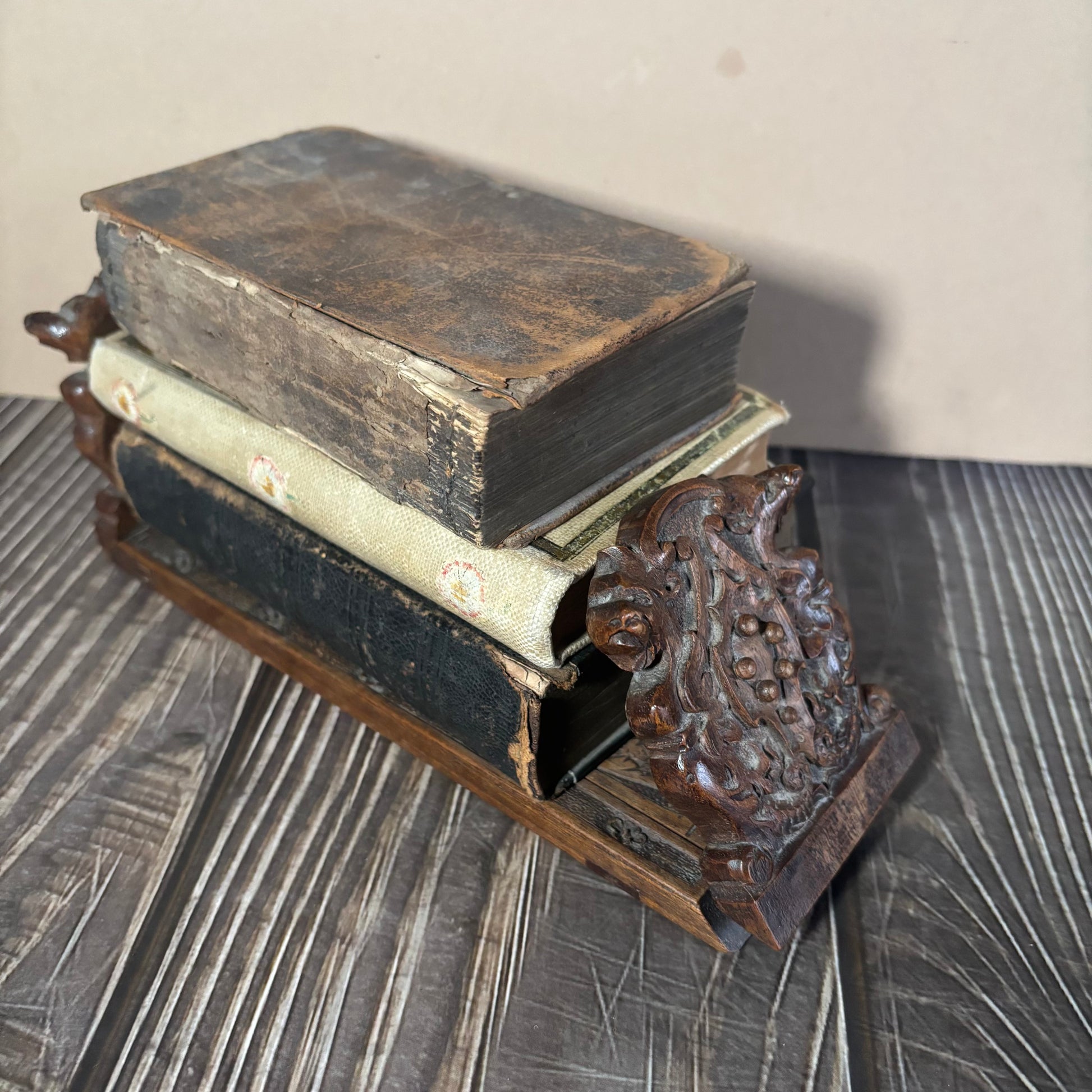 Stack of old books on a decorative wooden book stand with intricate designs.
