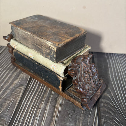 Stack of old books on a decorative wooden book stand with intricate designs.