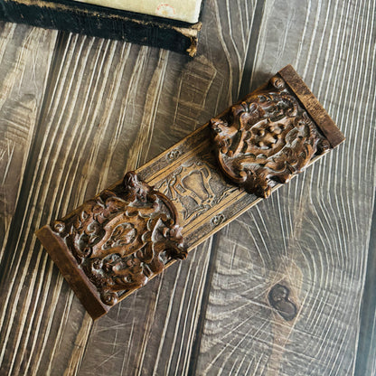 Decorative metal object with intricate designs on a textured wooden surface