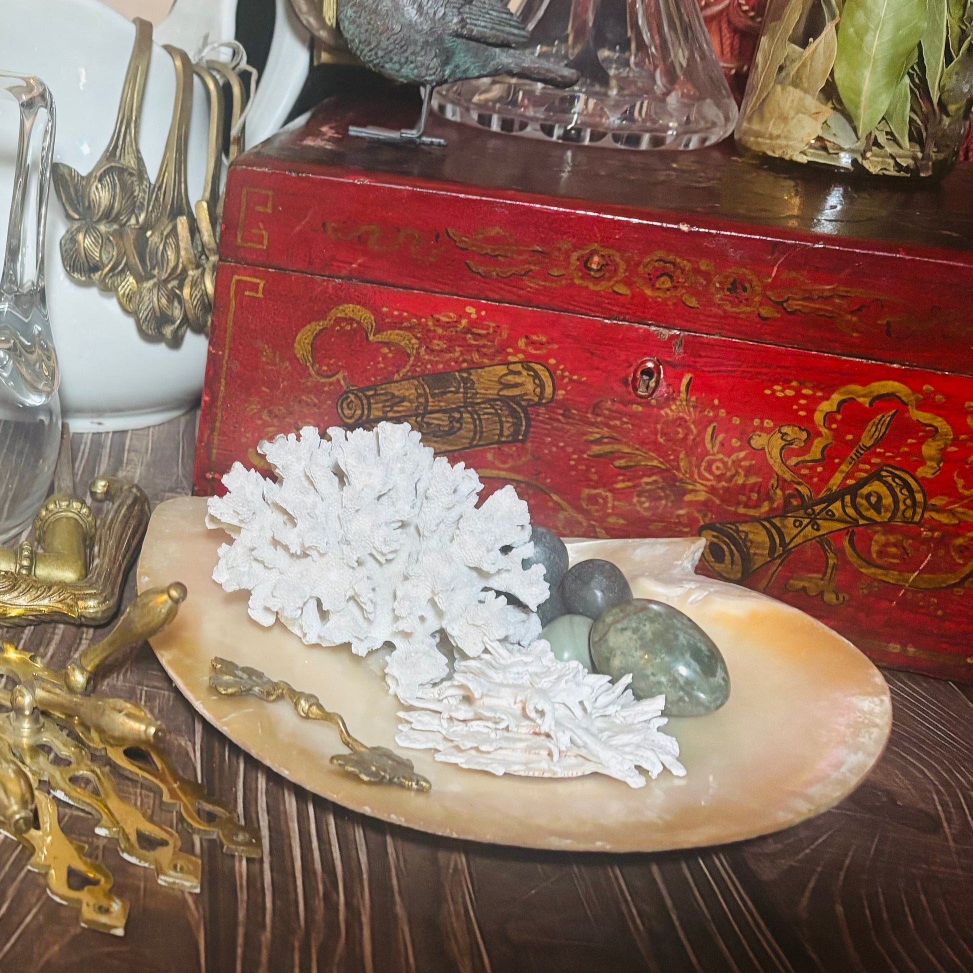 Decorative setting with white coral, green stones, and a red box with gold designs on a wooden surface.