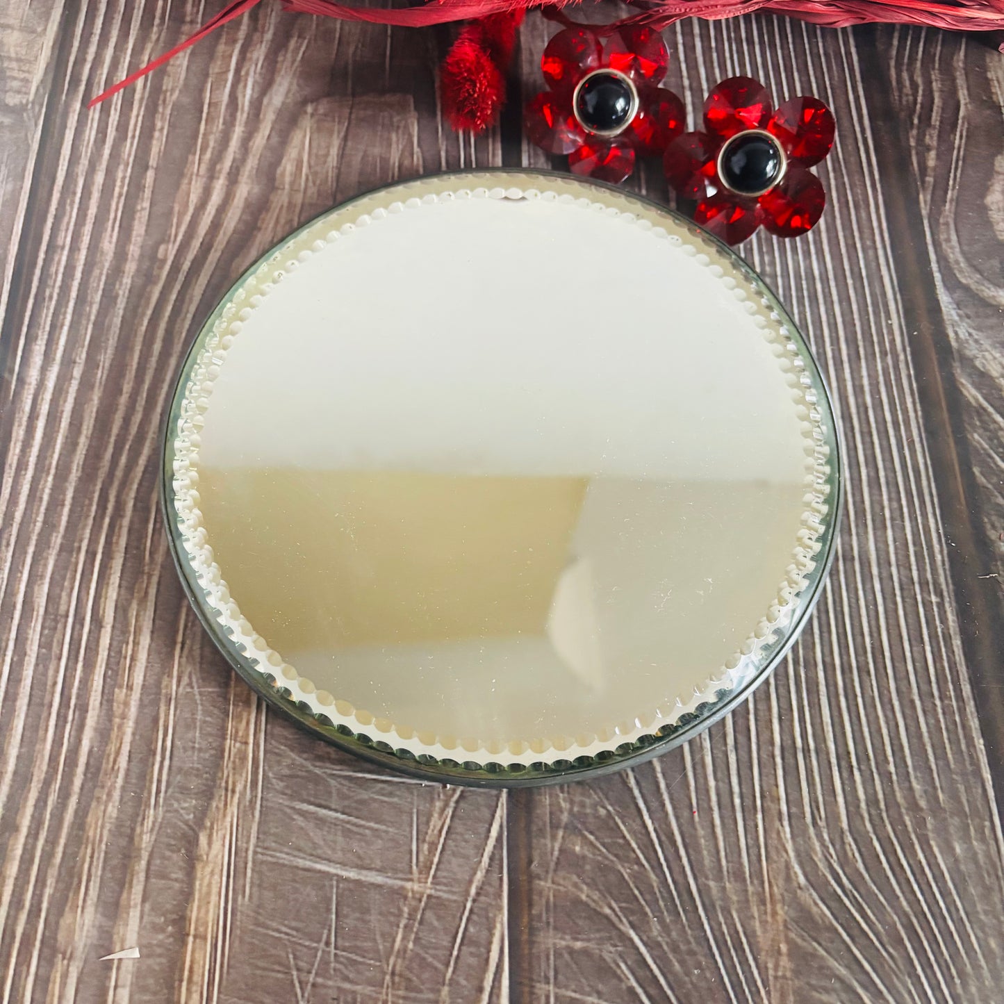Round mirror with decorative red flowers on a wooden surface