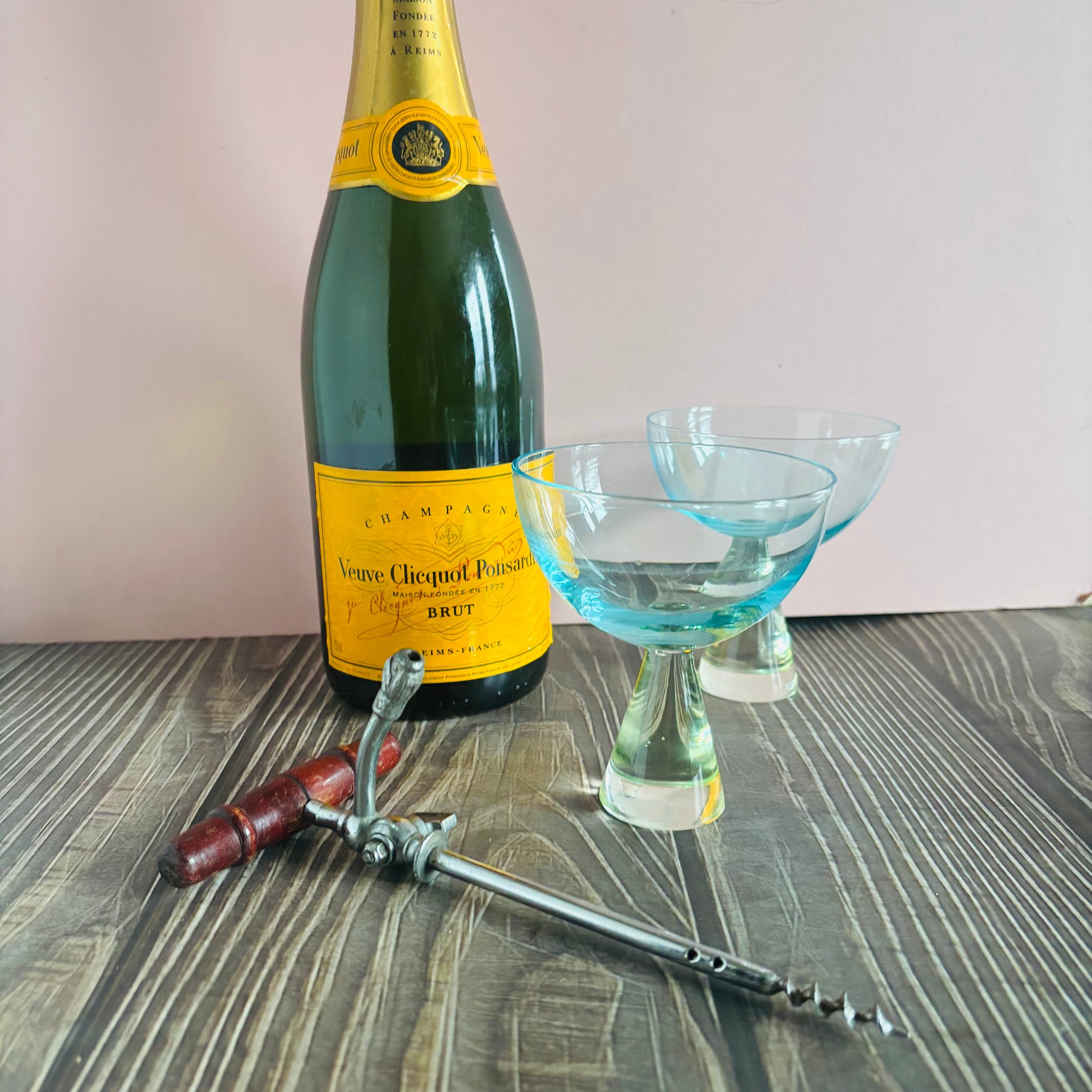 Bottle of Veuve Clicquot champagne with two cocktail glasses and a corkscrew on a wooden surface.