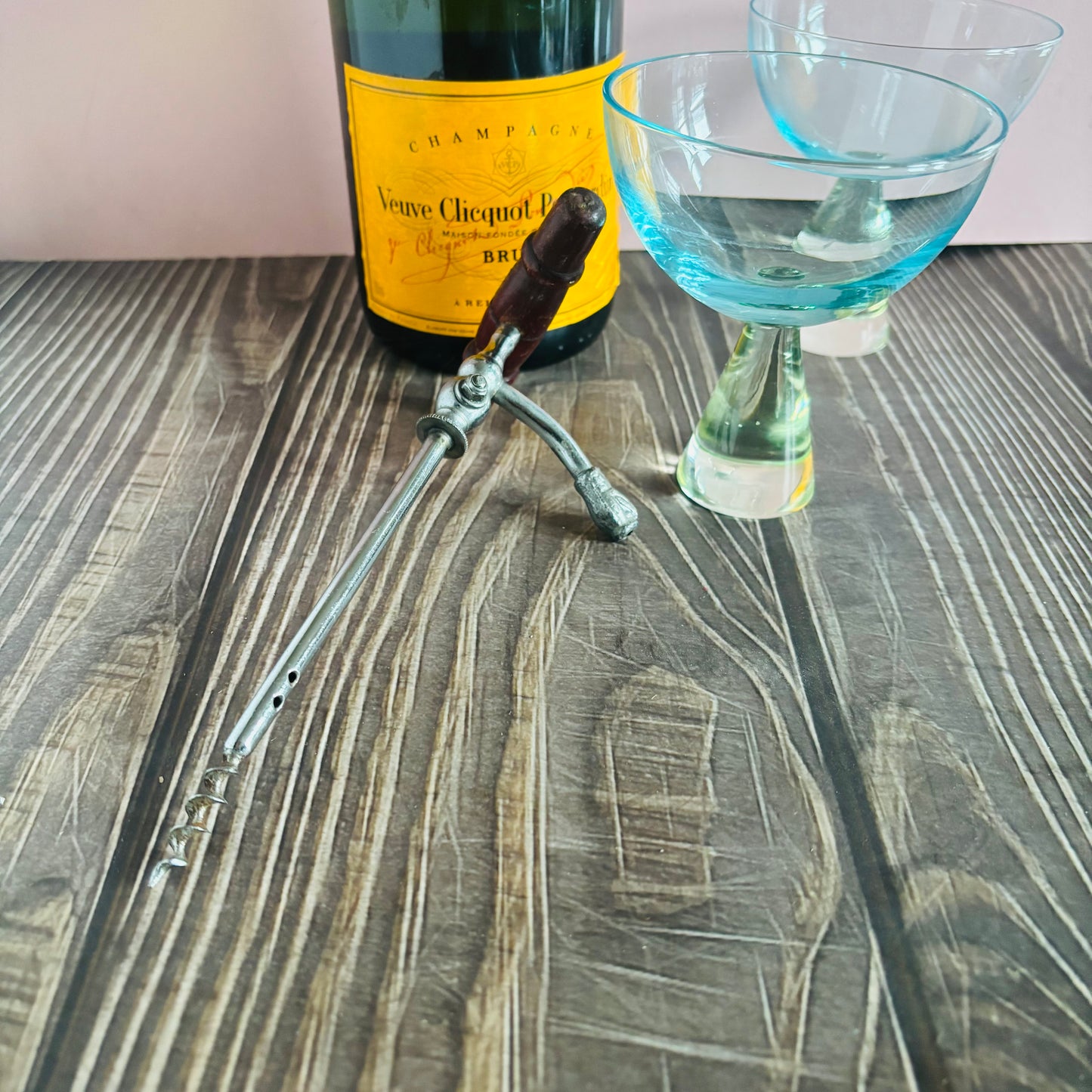 Bottle of Veuve Clicquot champagne with a corkscrew and a glass on a wooden surface.