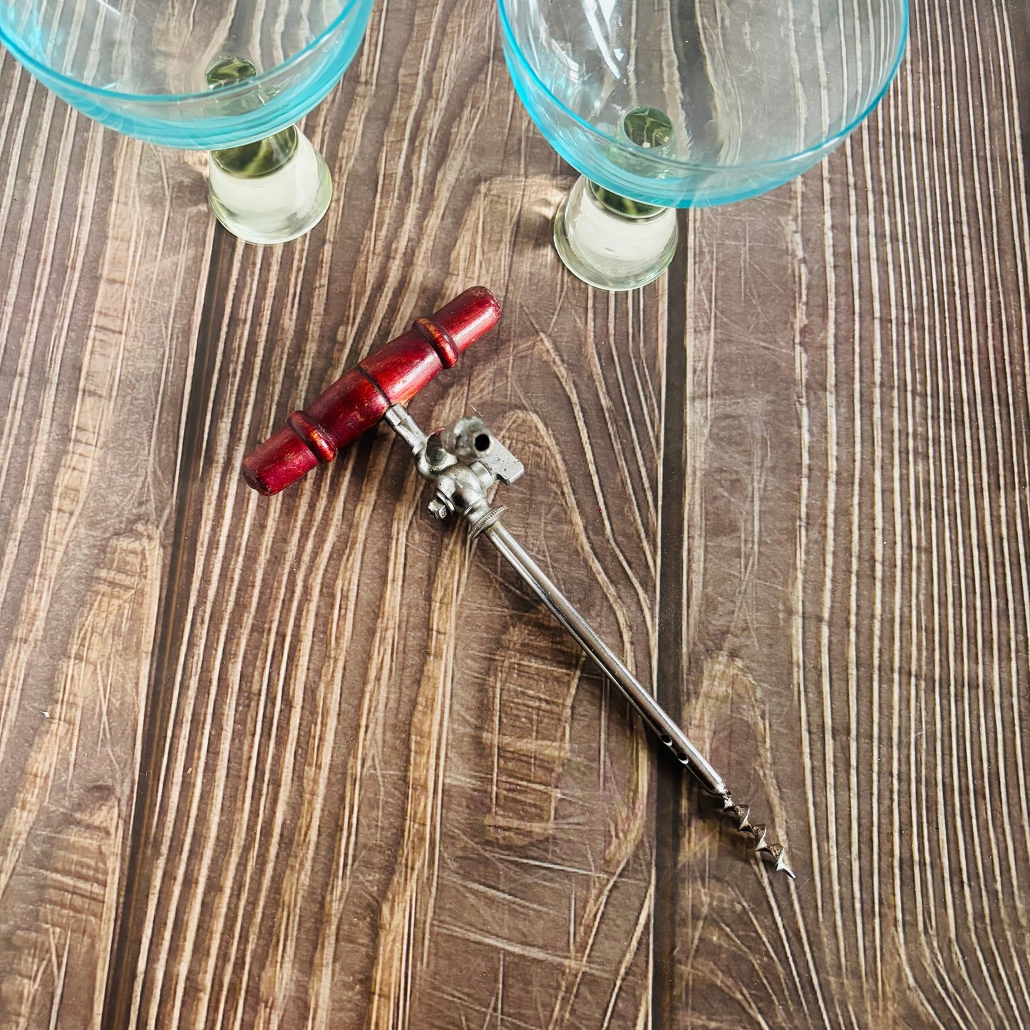 Bartending tool with red handle and silver body on a wooden surface with two glasses in the background.