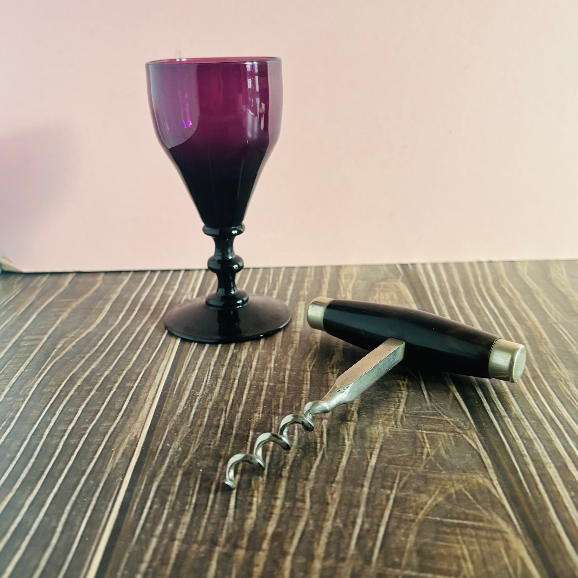 Amethyst glass, antique corkscrew, on a wooden surface.