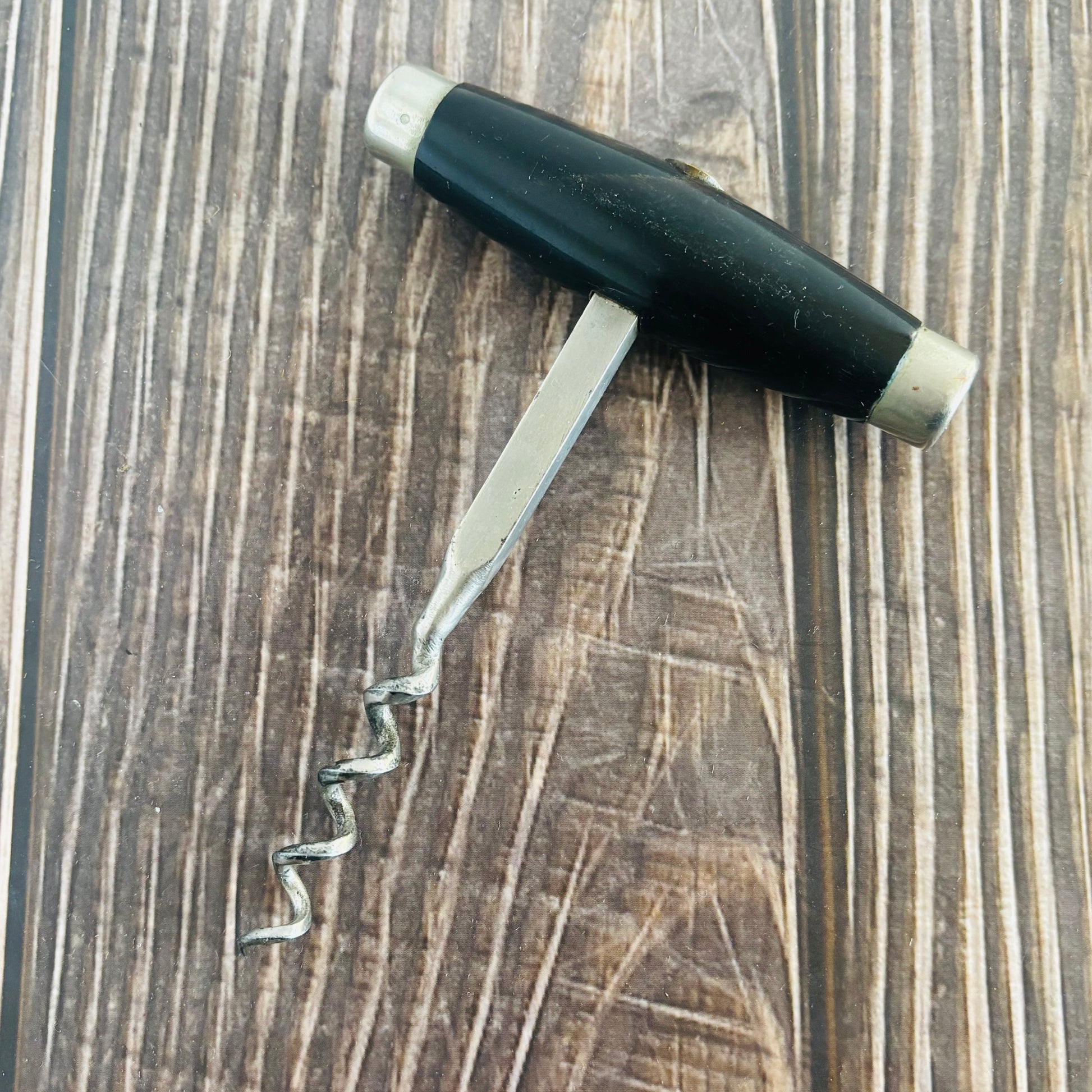 Corkscrew with black handle on a wooden surface