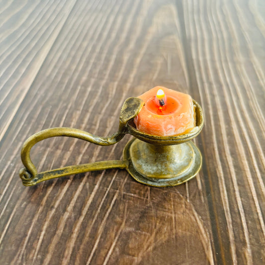 antique brass candle holder with a small candle on a wooden surface