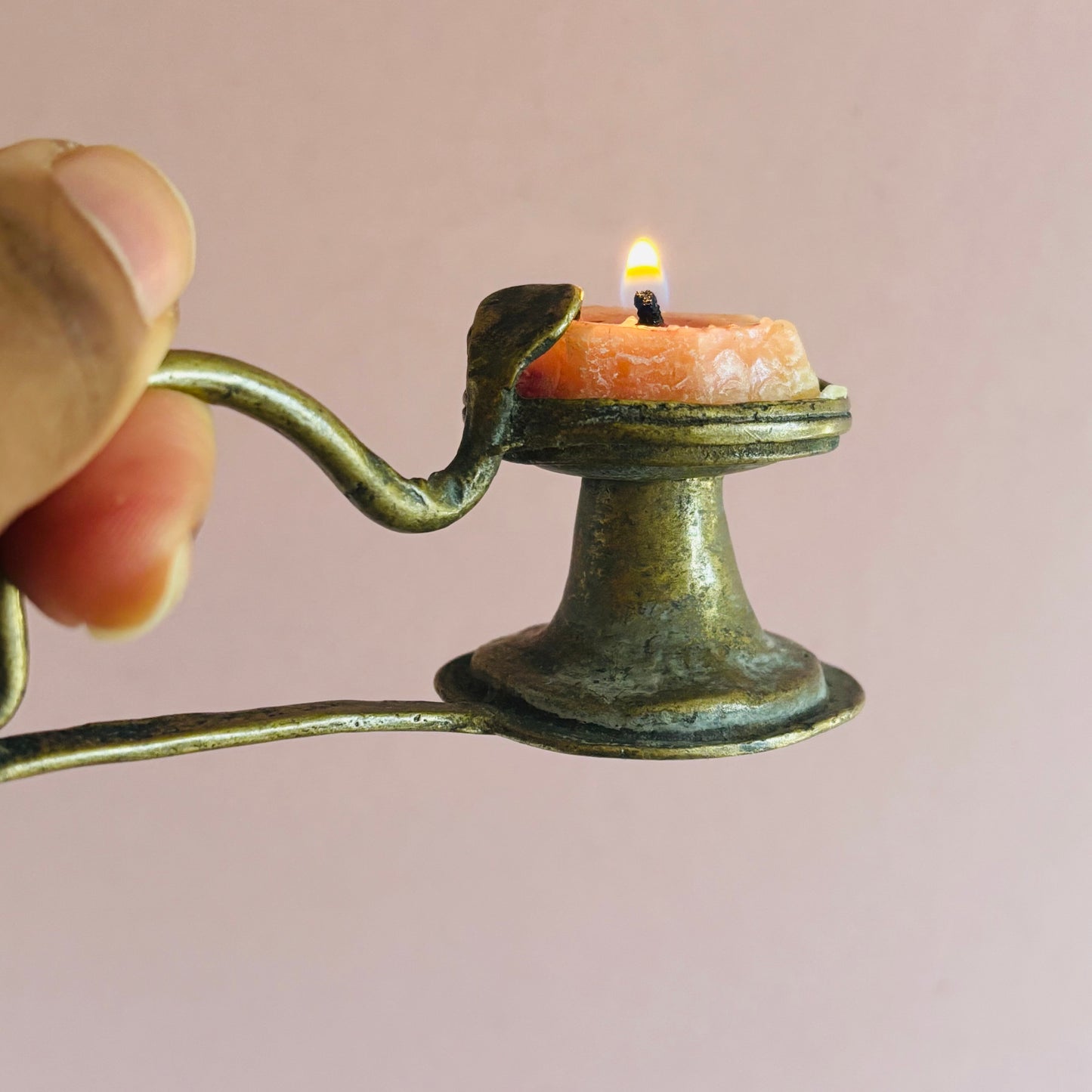 Hand holding a small bronze candle holder with a lit candle against a plain background