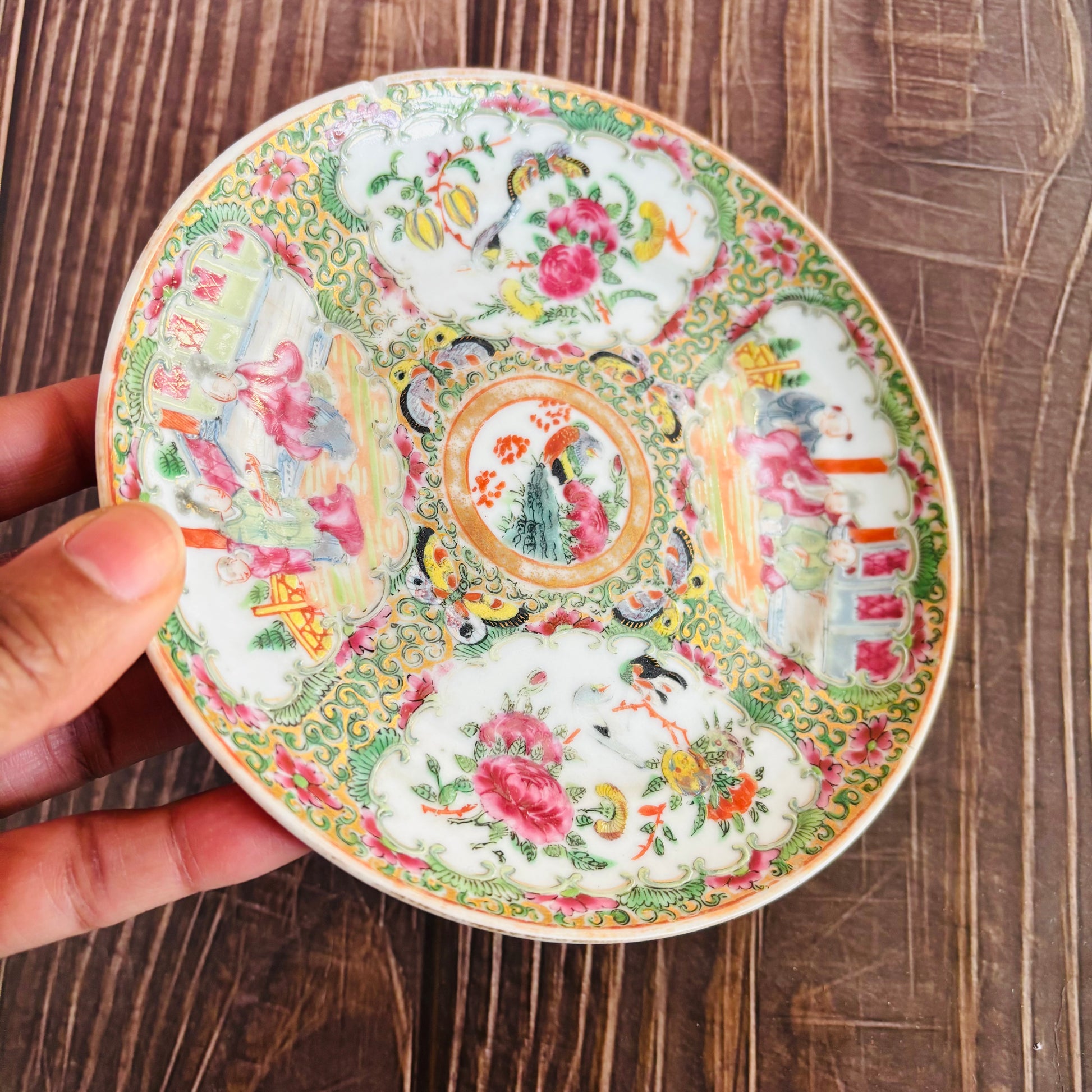 Decorative ceramic plate with intricate designs held by a hand on a wooden surface