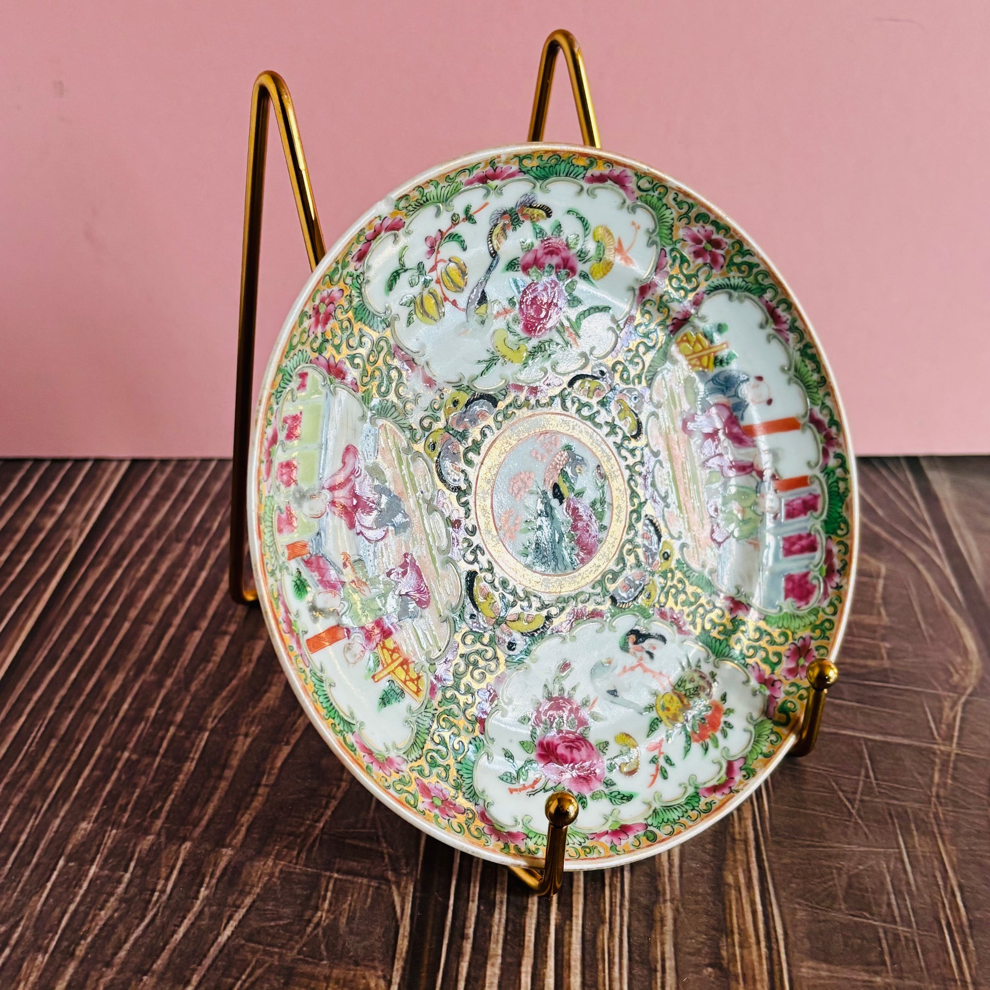 Decorative ceramic plate with intricate designs on a stand against a pink wall.